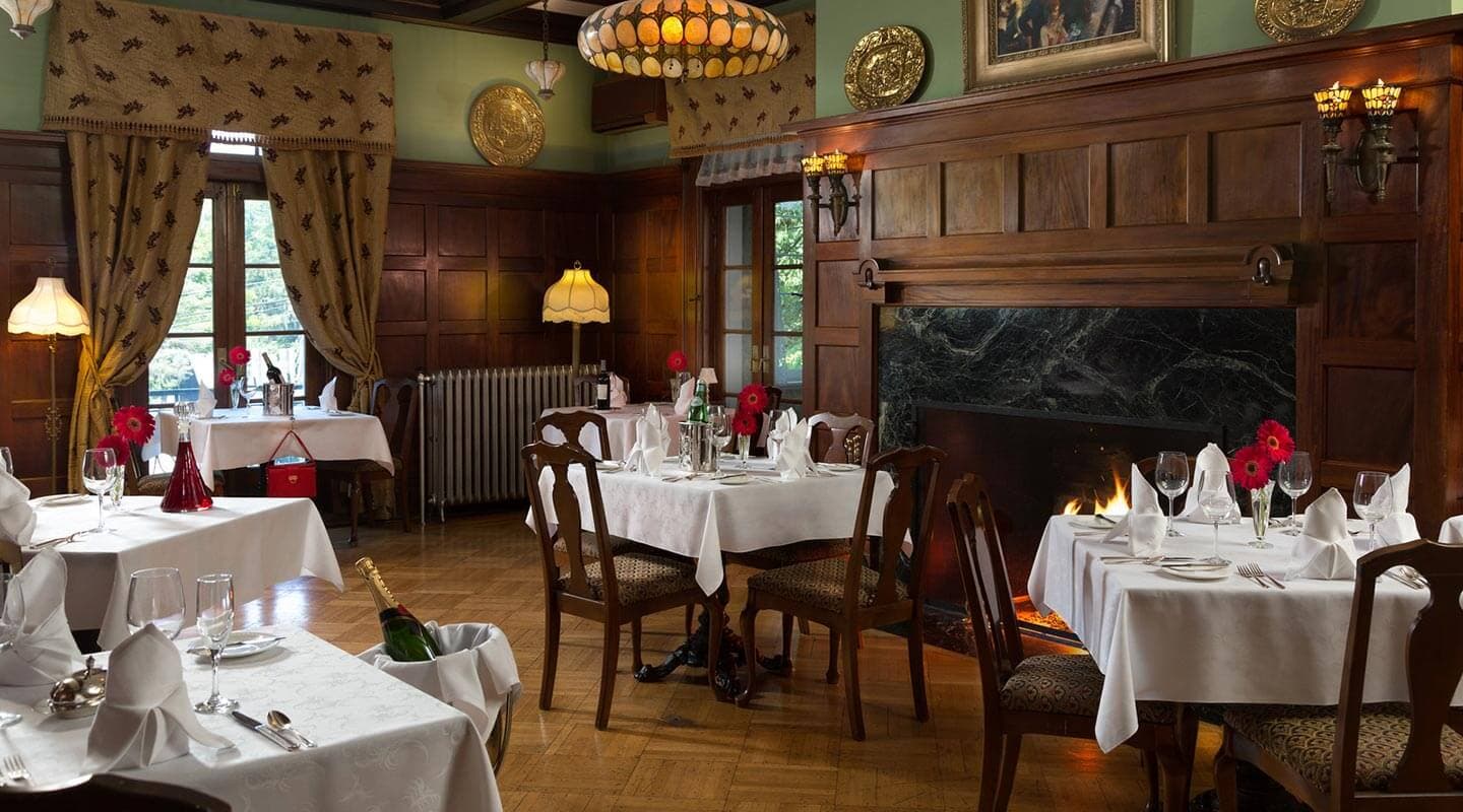 A cozy dining room with elegantly set tables, a fireplace, and soft lighting.
